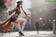 A woman in a brown dress and hat is dancing in the street.