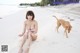 A woman in a pink bikini sitting on a beach next to a dog.