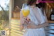 A woman in a white dress holding a glass of orange juice.