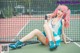 A woman with pink hair sitting on a tennis court.